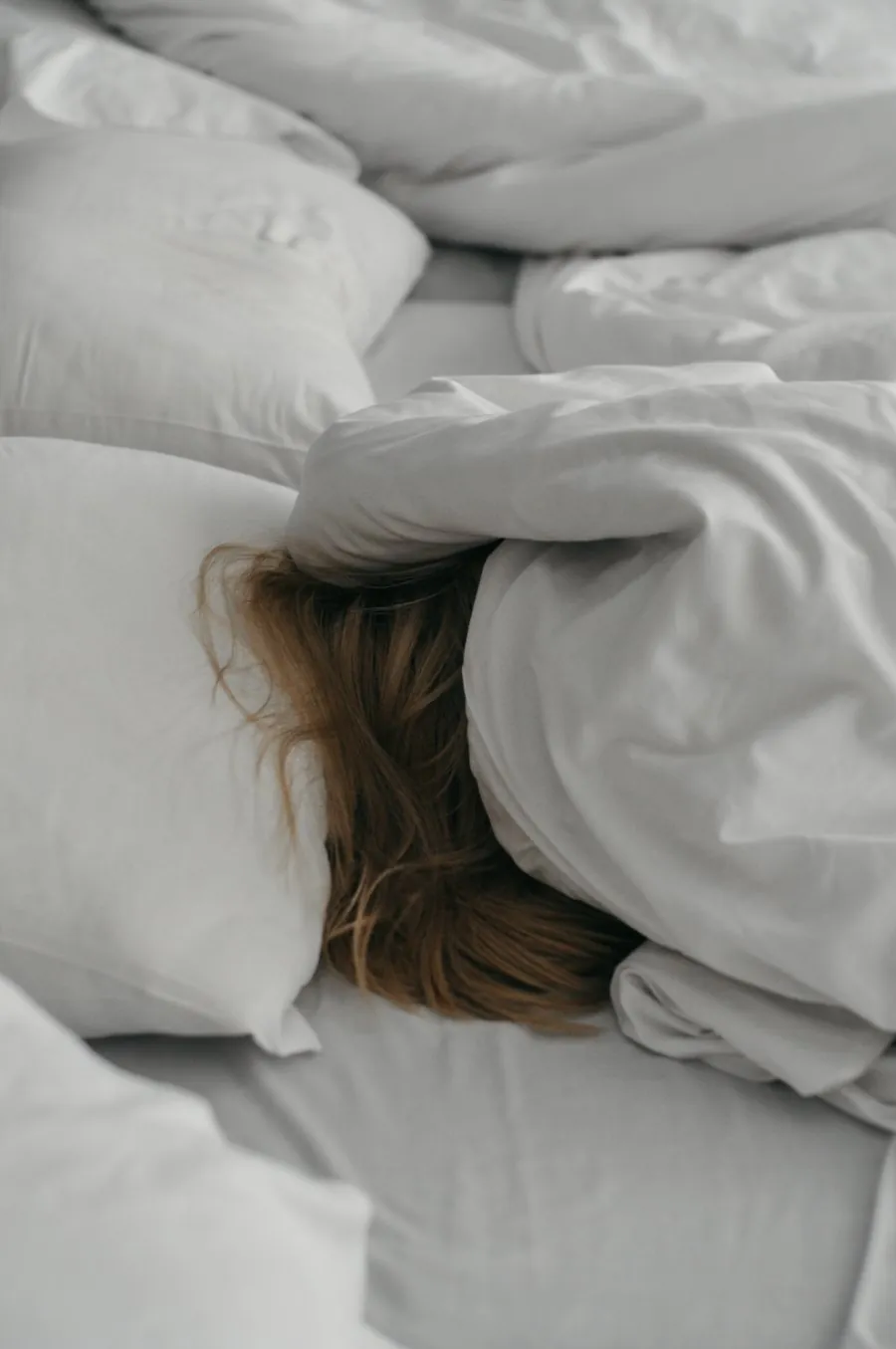 Woman hiding her head under the pillow to block out the snoring